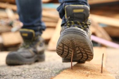 Careless worker stepping on nail in wooden plank outdoors, closeup