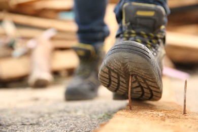 Careless worker stepping on nail in wooden plank outdoors, closeup. Space for text