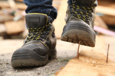 Photo of Careless worker stepping on nail in wooden plank outdoors, closeup