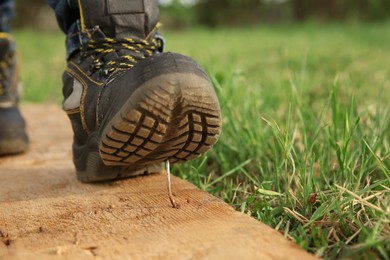 Photo of Careless worker stepping on nail in wooden plank outdoors, closeup