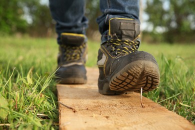 Careless worker stepping on nail in wooden plank outdoors, closeup