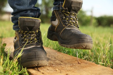 Photo of Careless worker stepping on nail in wooden plank outdoors, closeup