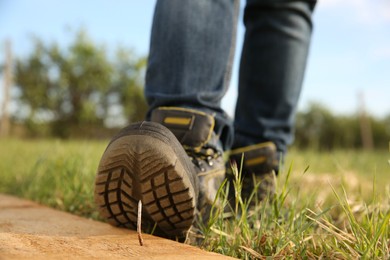 Photo of Careless worker stepping on nail in wooden plank outdoors, closeup