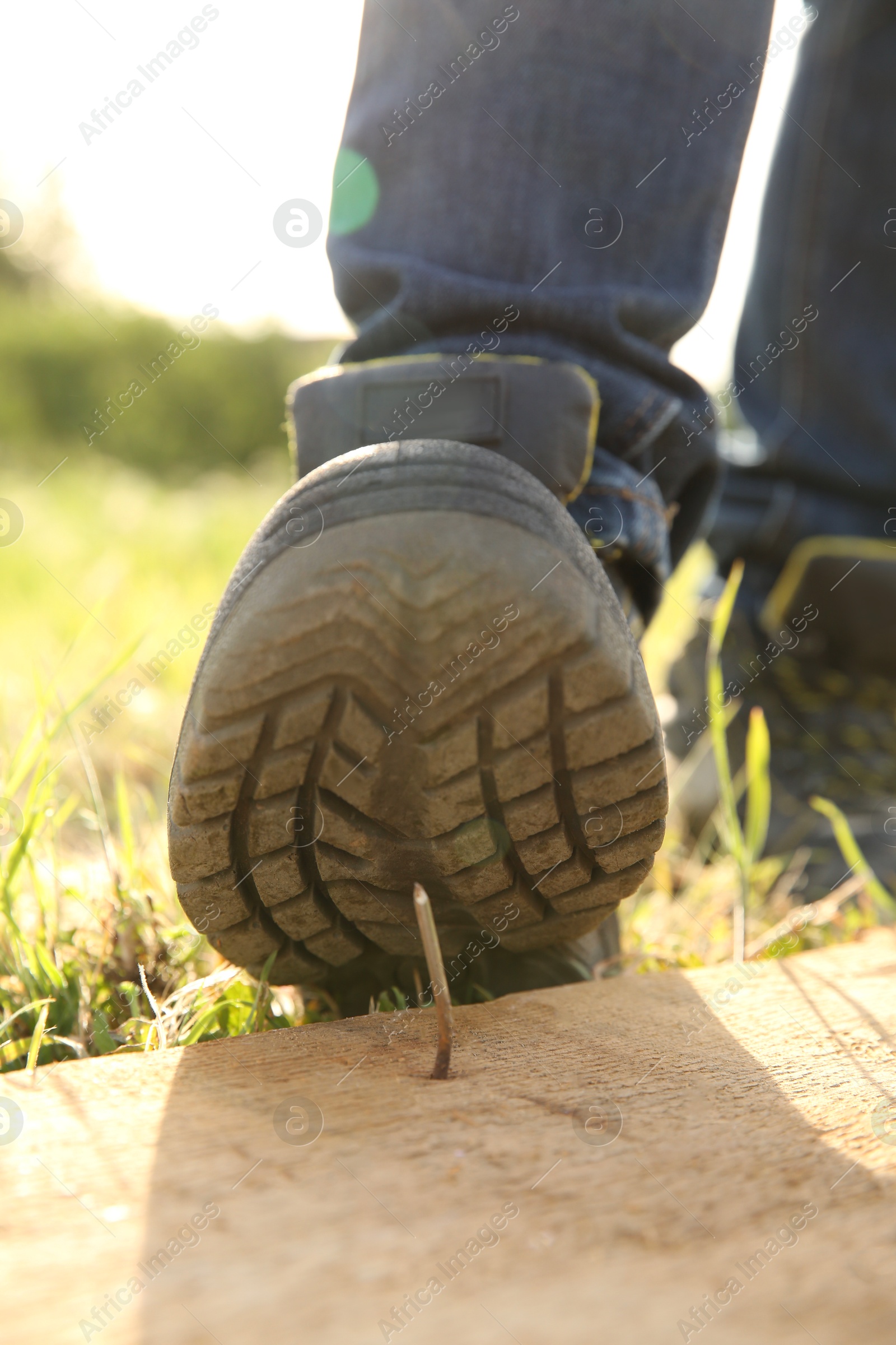 Photo of Careless worker stepping on nail in wooden plank outdoors, closeup