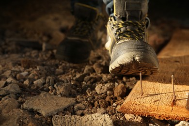 Careless worker stepping on nail in wooden plank, closeup. Space for text