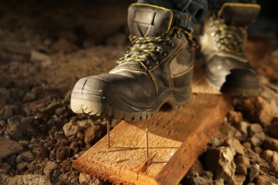 Photo of Careless worker stepping on nails in wooden plank, closeup