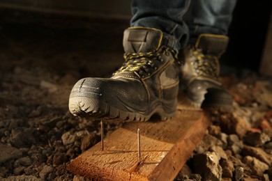 Photo of Careless worker stepping on nails in wooden plank, closeup