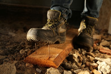 Photo of Careless worker stepping on nails in wooden plank, closeup