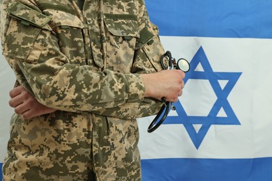 Photo of Man in military uniform with crossed arms and stethoscope against flag of Israel, closeup. Health care concept