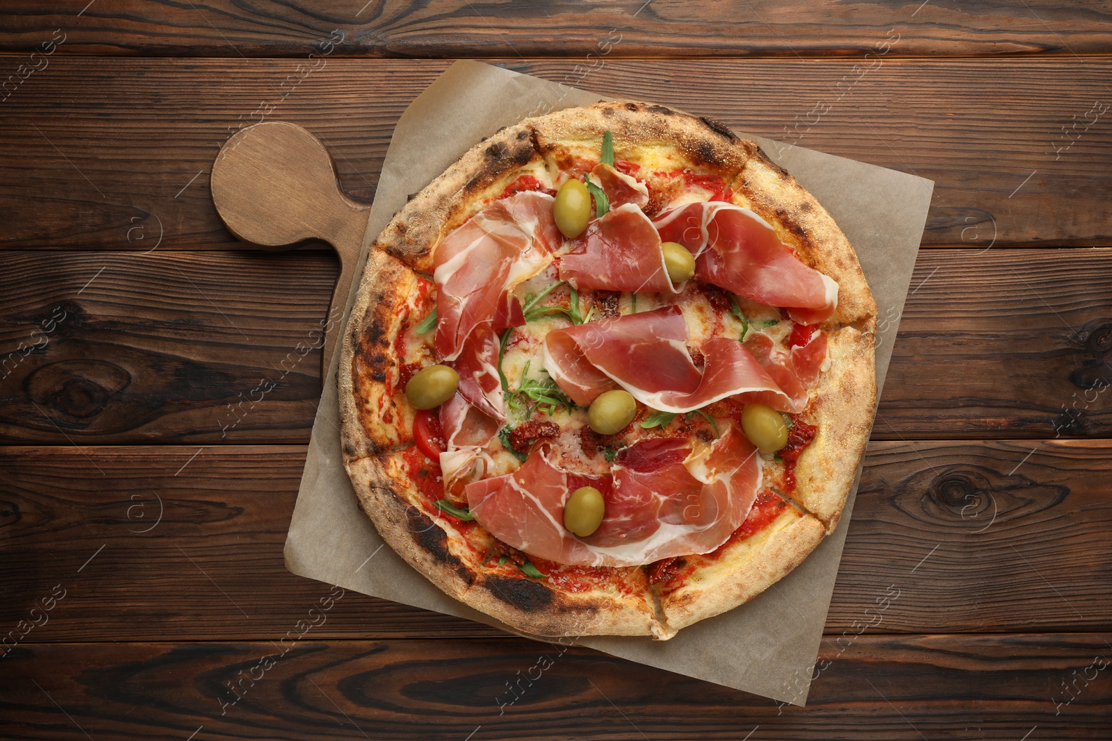 Photo of Tasty pizza with cured ham, olives and sun-dried tomato on wooden table, top view