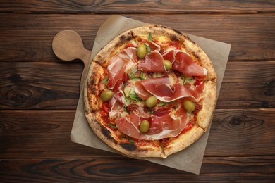 Photo of Tasty pizza with cured ham, olives and sun-dried tomato on wooden table, top view