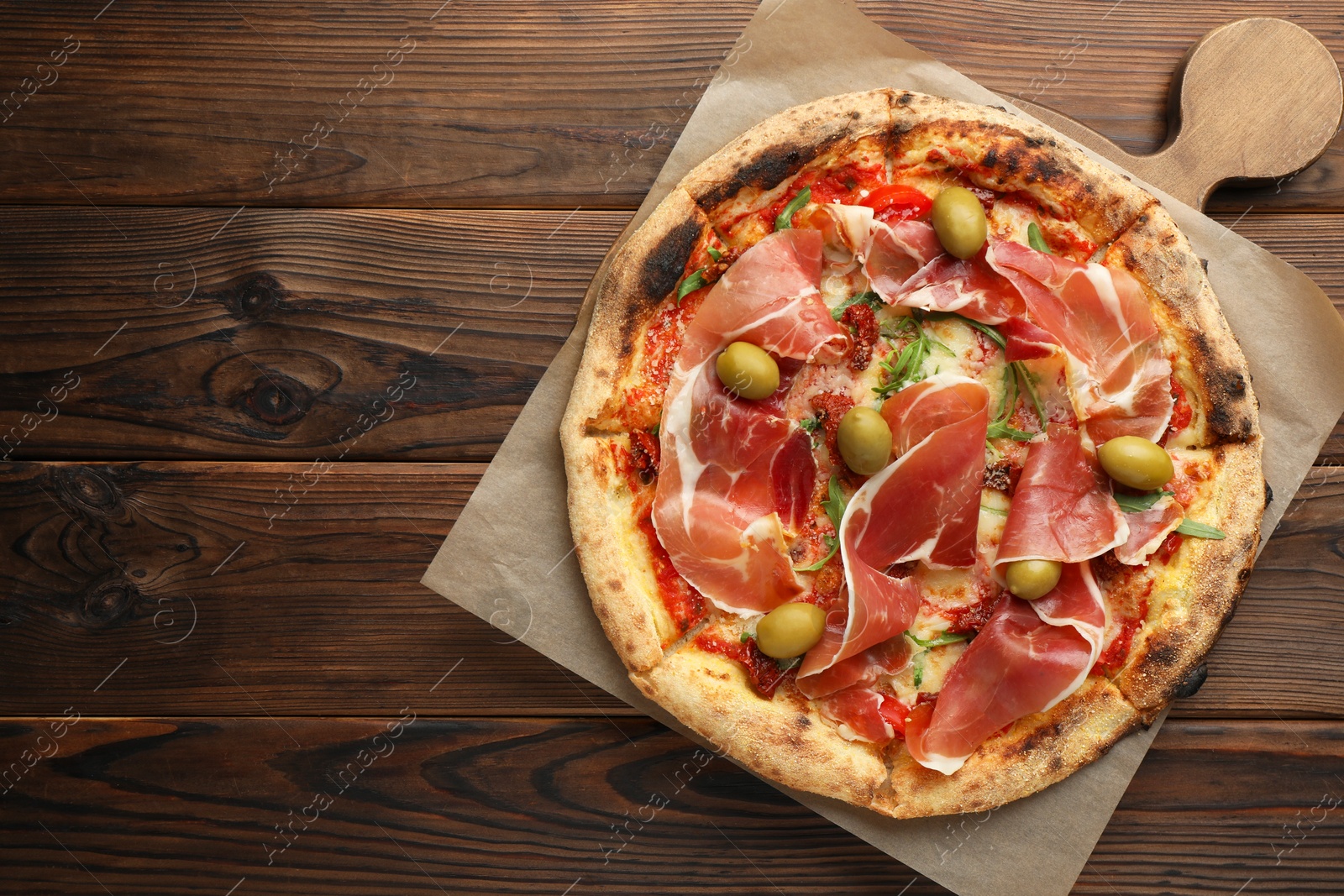 Photo of Tasty pizza with cured ham, olives and sun-dried tomato on wooden table, top view. Space for text