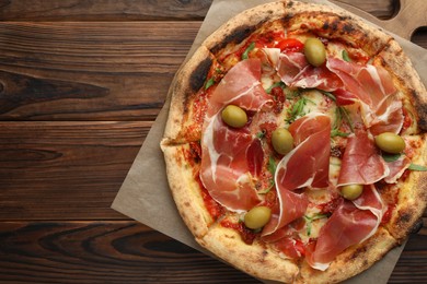 Photo of Tasty pizza with cured ham, olives and sun-dried tomato on wooden table, top view. Space for text