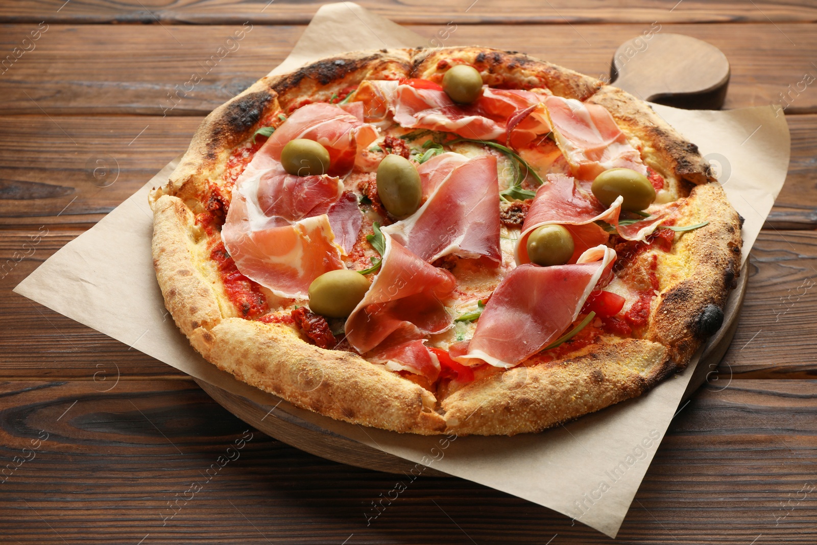 Photo of Tasty pizza with cured ham, olives and sun-dried tomato on wooden table