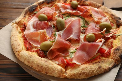 Photo of Tasty pizza with cured ham, olives and sun-dried tomato on wooden table, closeup