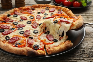 Photo of Taking piece of tasty pizza at wooden table, closeup