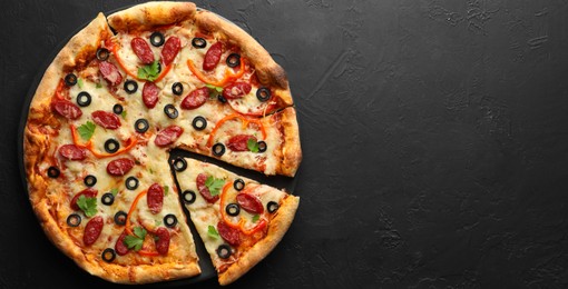 Photo of Tasty pizza with dry smoked sausages, olives, pepper and parsley on black table, top view. Space for text