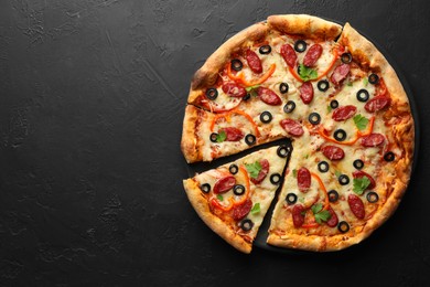 Photo of Tasty pizza with dry smoked sausages, olives, pepper and parsley on black table, top view. Space for text