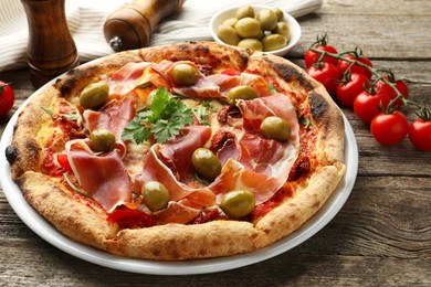 Tasty pizza with cured ham, olives, tomatoes and parsley on wooden table