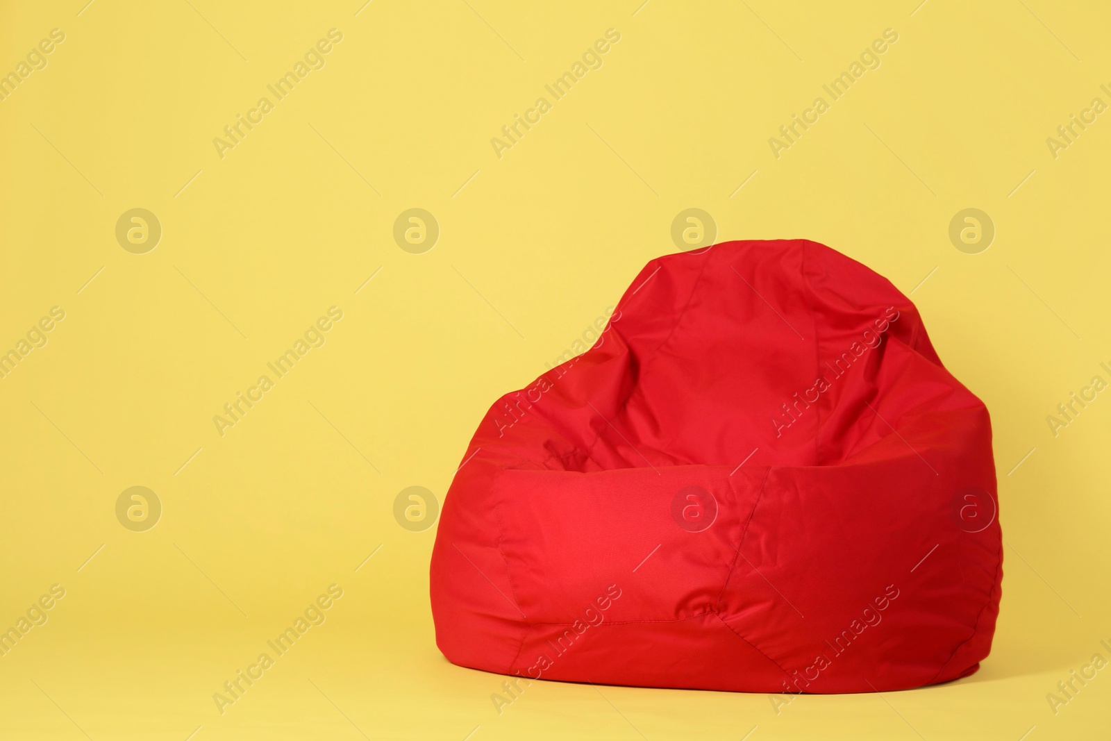 Photo of Red bean bag chair on yellow background, space for text