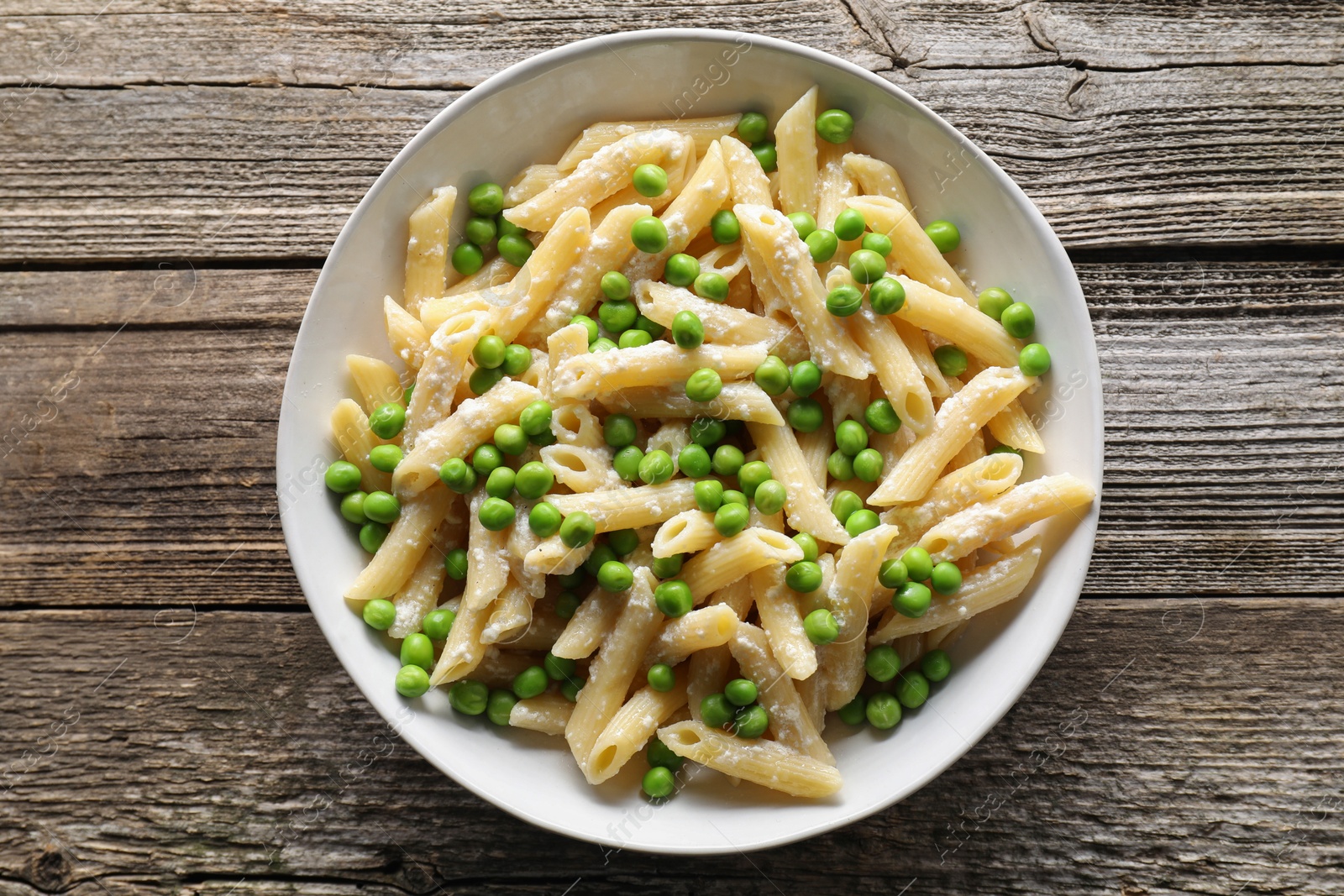 Photo of Delicious pasta with green peas and cheese in bowl on wooden table, top view