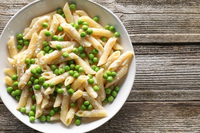 Delicious pasta with green peas and cheese in bowl on wooden table, top view. Space for text