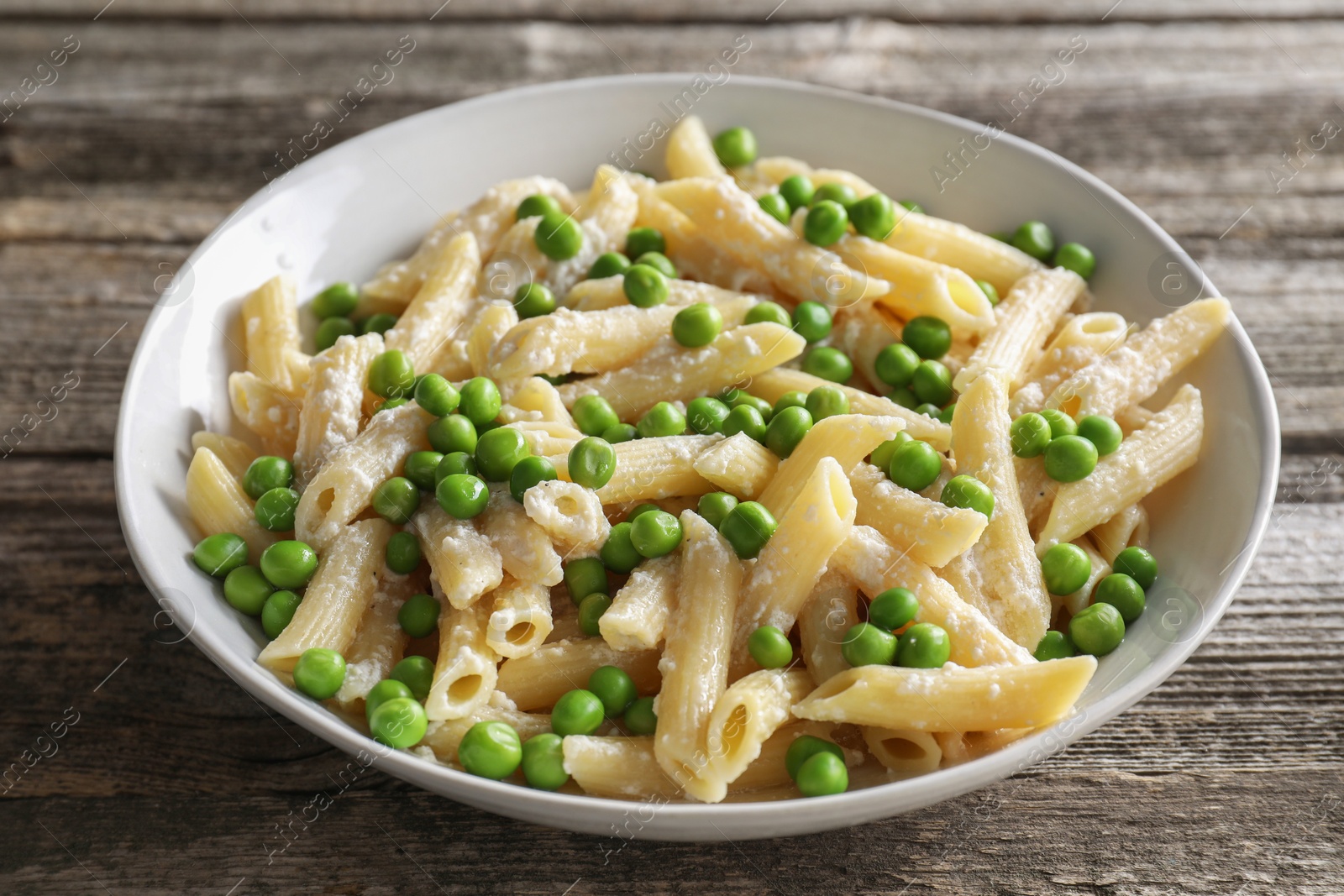 Photo of Delicious pasta with green peas and cheese in bowl on wooden table