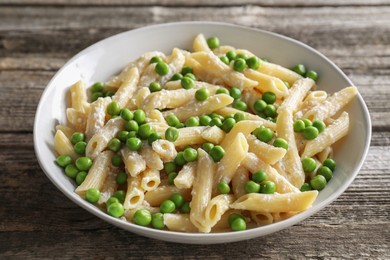 Delicious pasta with green peas and cheese in bowl on wooden table