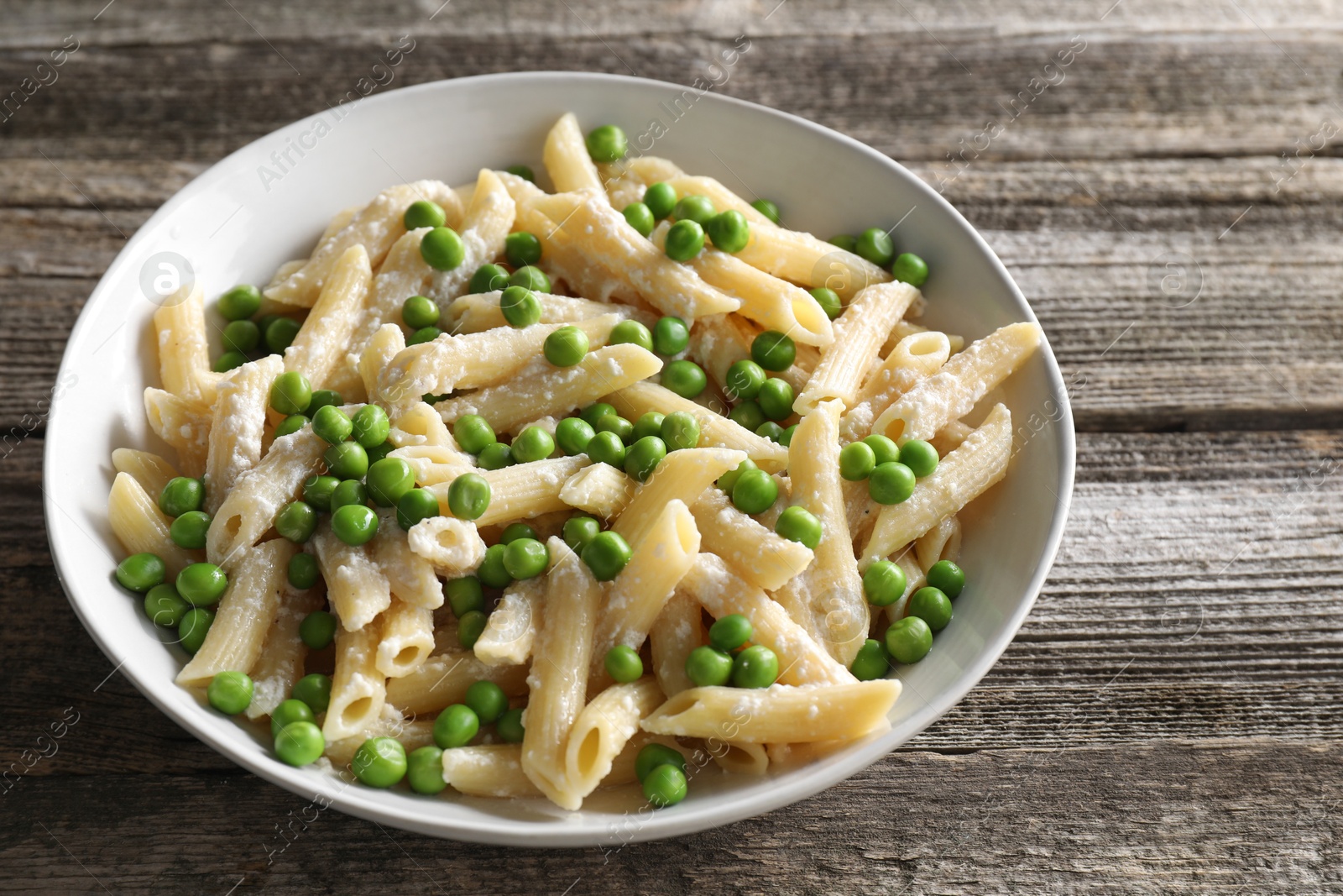 Photo of Delicious pasta with green peas and cheese in bowl on wooden table