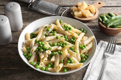 Photo of Delicious pasta with green peas, cheese, grater and fork on wooden table