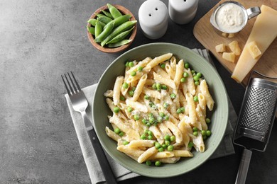 Photo of Delicious pasta with green peas served on grey table, top view