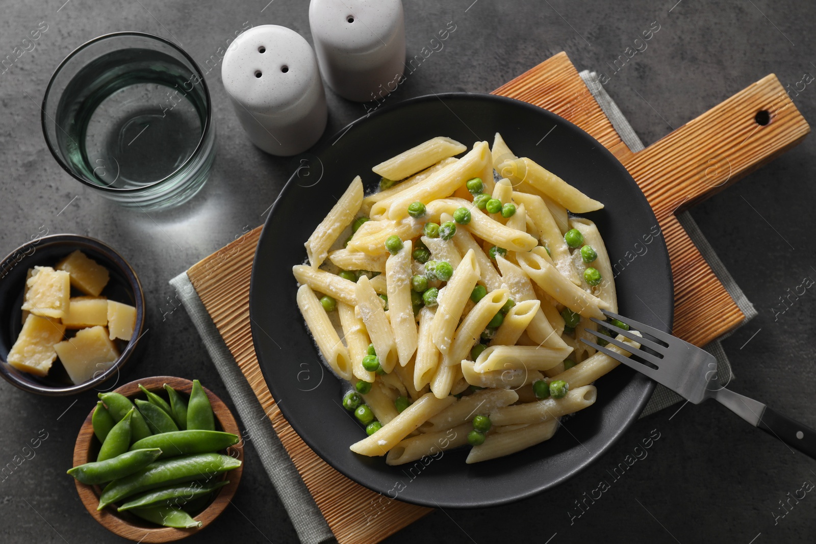 Photo of Delicious pasta with green peas, cheese, fork and water on grey table, top view