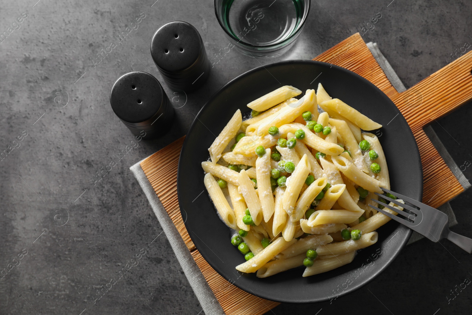 Photo of Delicious pasta with green peas, cheese, fork and water on grey table, top view. Space for text