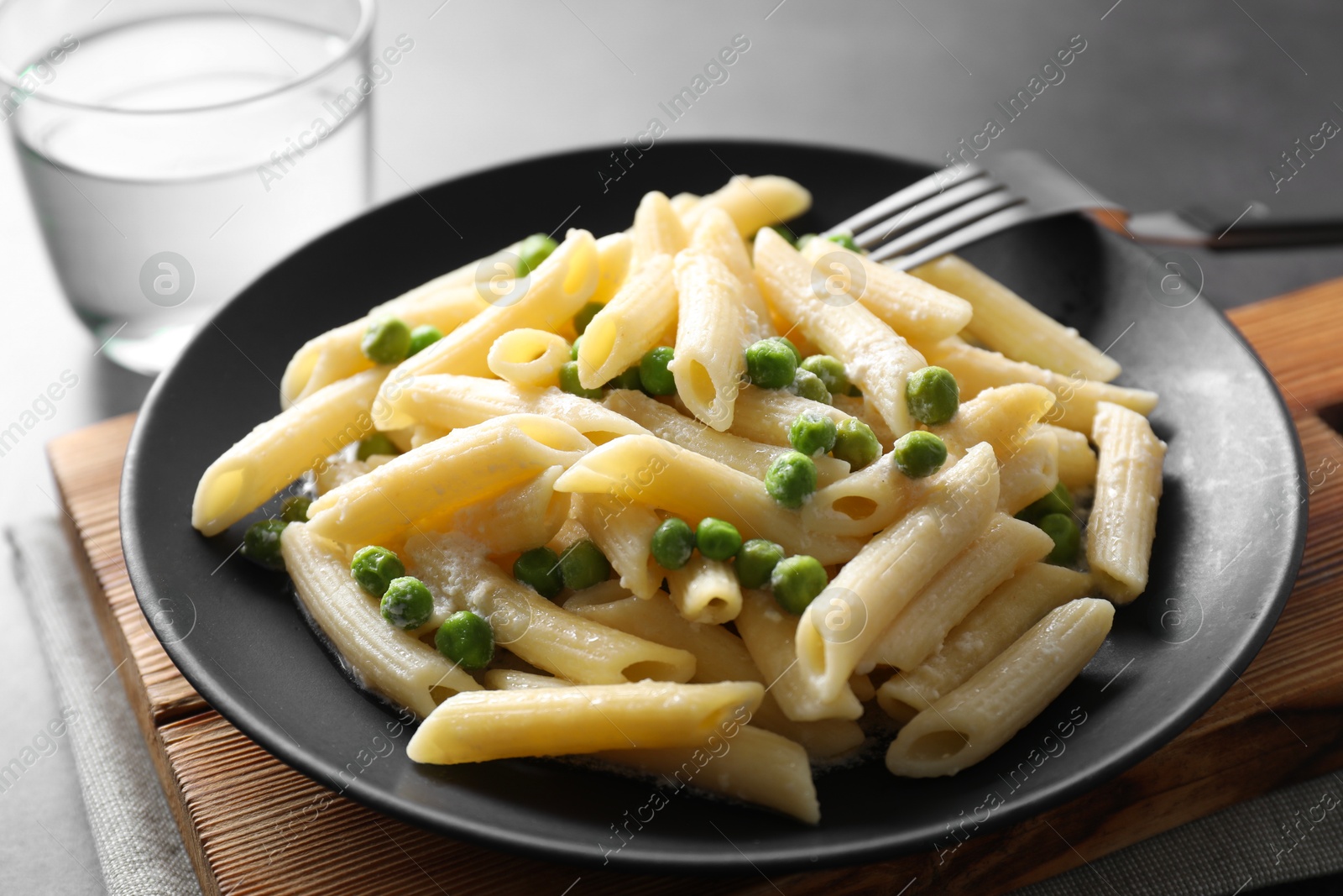 Photo of Delicious pasta with green peas, cheese, fork and water on table