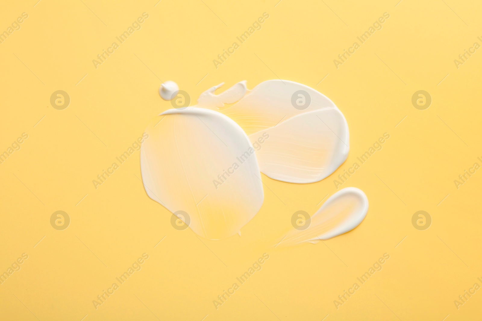 Photo of Samples of face cream on yellow background, top view