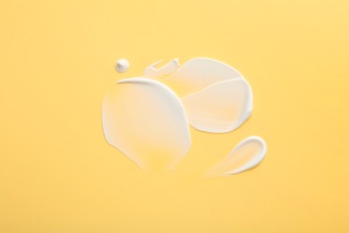 Photo of Samples of face cream on yellow background, top view