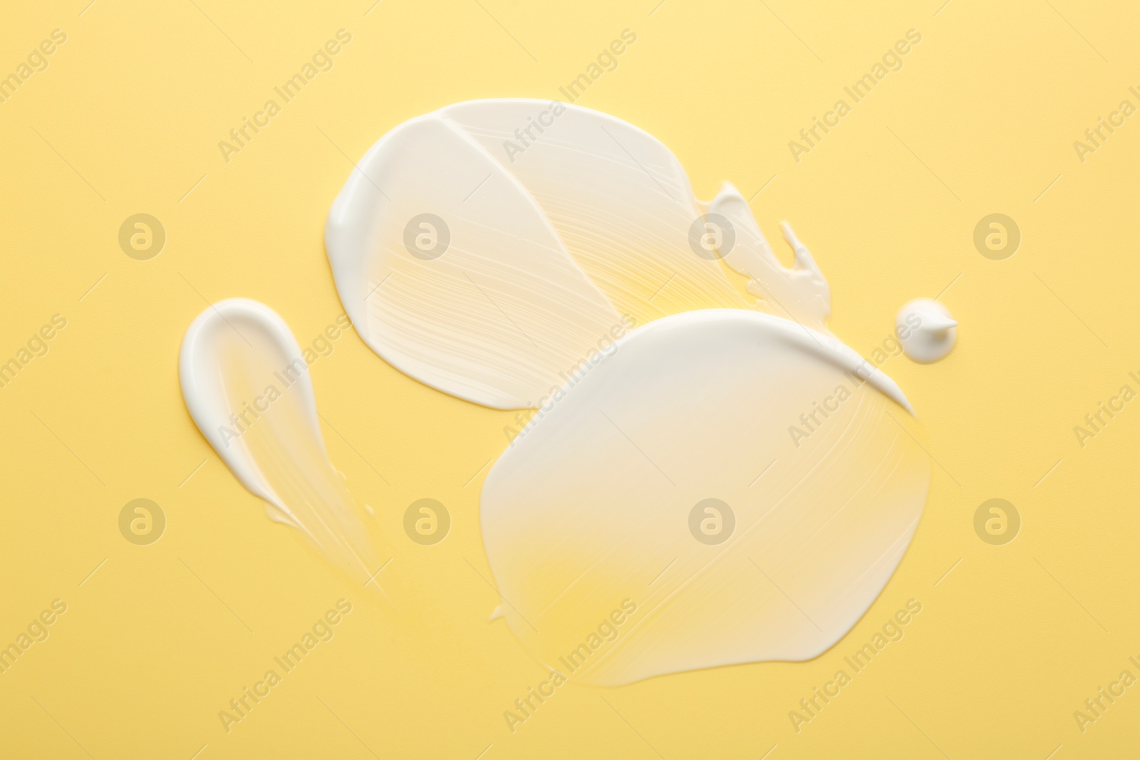 Photo of Samples of face cream on yellow background, top view