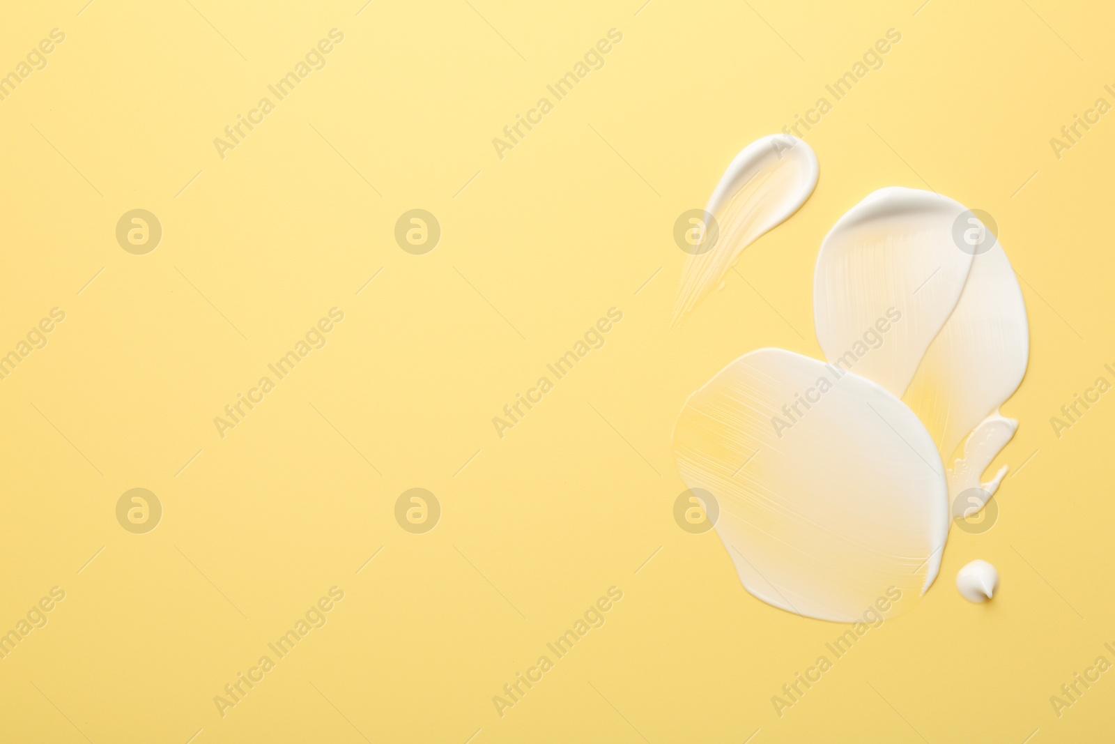 Photo of Samples of face cream on yellow background, top view. Space for text