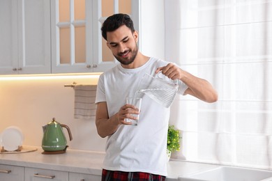 Photo of Morning of happy man pouring water from jug into glass in kitchen