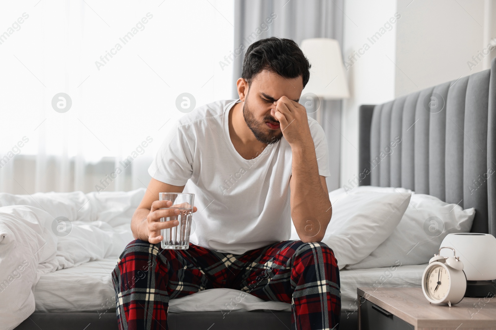 Photo of Man suffering from headache with glass of water on bed at morning