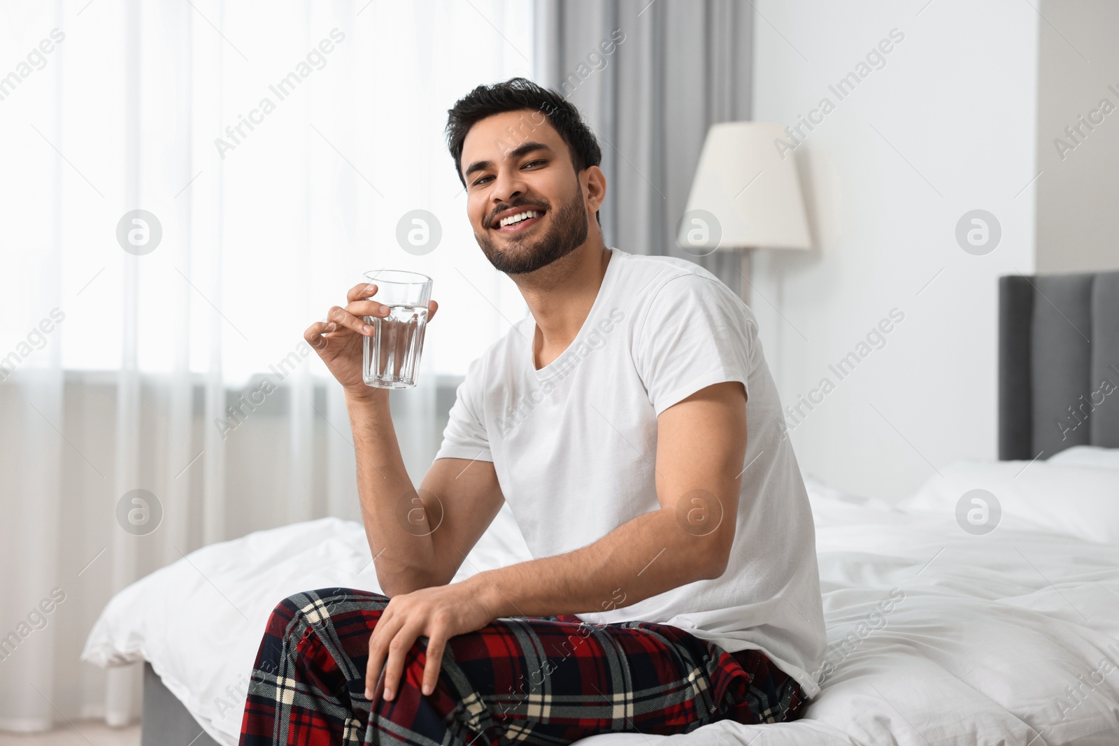 Photo of Happy man with glass of water on bed at morning