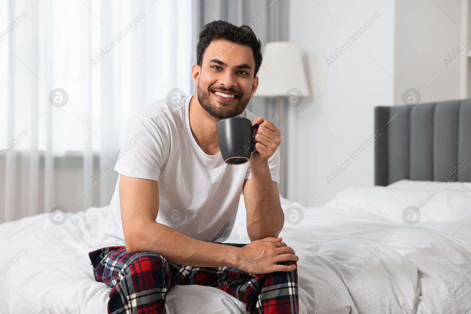 Photo of Happy man with cup of coffee on bed at morning