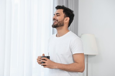 Photo of Happy man with cup of morning coffee at home. Space for text