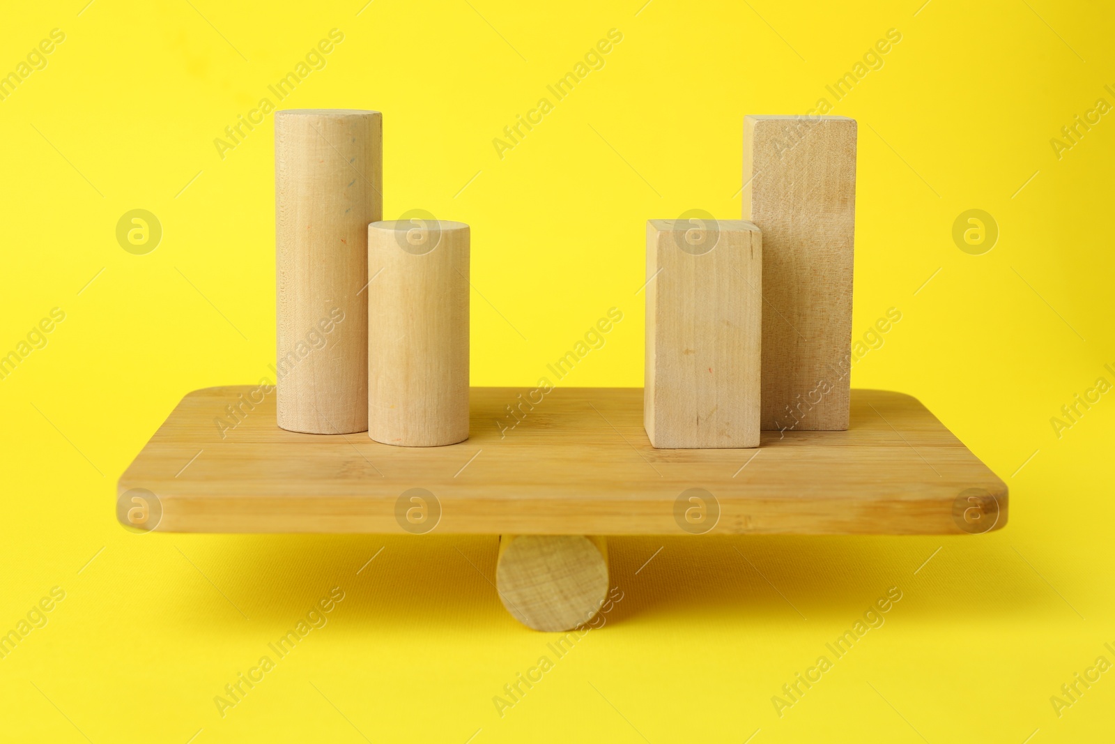 Photo of Equality concept. Balance scale with different wooden blocks on yellow background