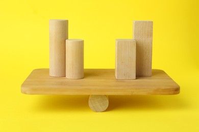 Equality concept. Balance scale with different wooden blocks on yellow background