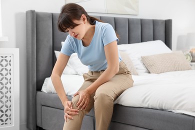 Photo of Upset woman suffering from knee pain on bed at home