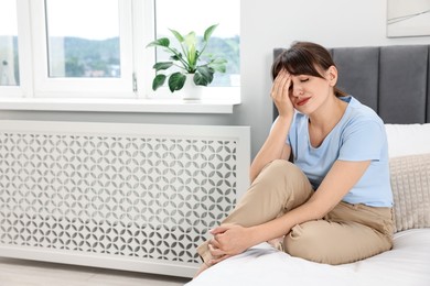 Photo of Upset woman suffering from headache on bed at home, space for text