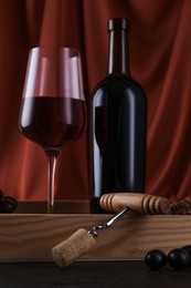 Corkscrew, glass of wine, bottle and grapes on table