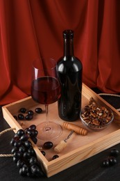 Corkscrew, glass of wine, bottle and grapes on black table