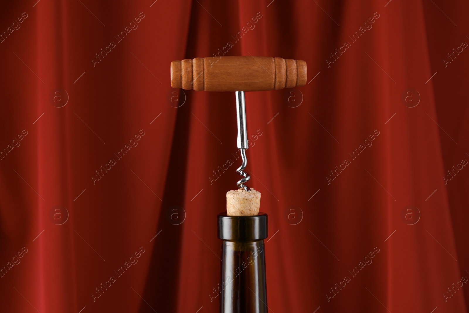 Photo of Wine bottle with corkscrew on red background, closeup